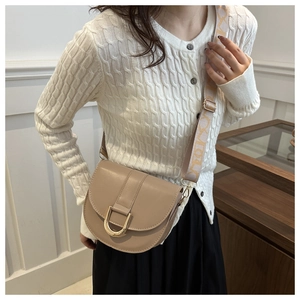 Detail of beige saddle bag with gold horseshoe buckle and patterned wide strap