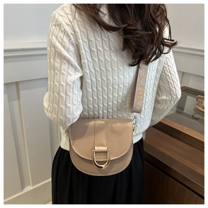 Detail of saddle bag showing beige PU leather texture and embroidered wide strap