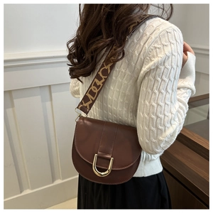 Close-up of brown leather saddle bag featuring a gold horseshoe buckle and jacquard strap