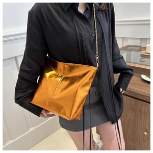 Detail of a metallic gold tote bag with a sleek chain strap worn over a black outfit