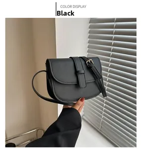 Detail view of a black semi-circular crossbody bag with golden buckle and matte leather