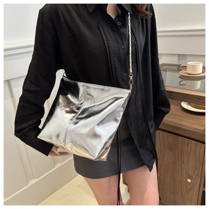 Detail shot of silver metallic bucket bag with golden chain strap on a glass table