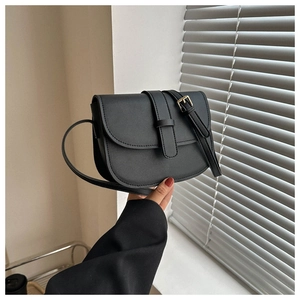 Close-up of black leather saddle bag with gold metal buckle held in a minimalist room