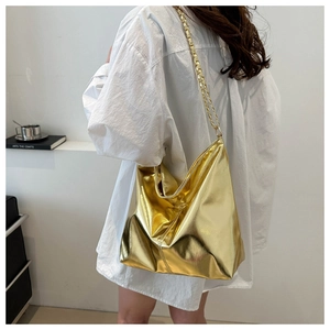 Model wearing a large golden hobo bag with a metallic finish and chain strap details
