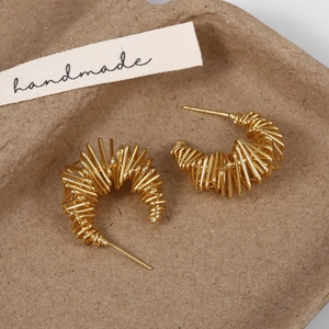 Macro shot of gold-plated twisted wire C-shaped earrings on a natural textured tray