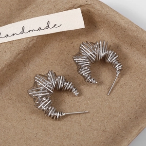Close-up of silver-tone intertwined wire C-shaped earrings on a handmade paper tray