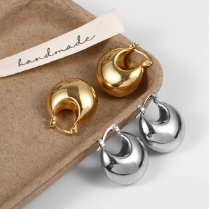 Close-up of minimalist gold and silver teardrop earrings on a handmade paper tray