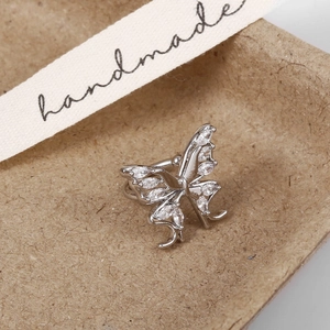 Macro shot of silver butterfly ear cuff with sparkling zircon inlay on textured paper