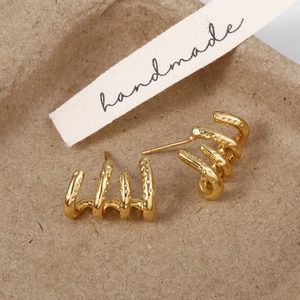 Gros plan de boucles d'oreilles dorées avec texture martelée et design à quatre griffes