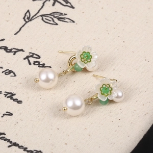 Dettaglio di orecchini di perle con fiore di trifoglio bianco e piccoli accenti verdi
