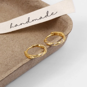 Close-up of gold twist hoop earrings with white zircon on a handmade display tray