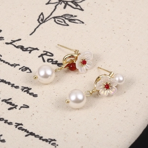 Dettaglio di orecchini a fiore vintage con perla e gemma rossa su sfondo di lino