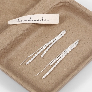 Detailed close-up of silver tassel threader earrings featuring refined starry textures