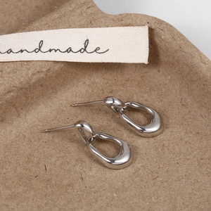 Close-up of silver oval hoop earrings on a textured tray with a handmade ribbon