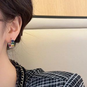 Elegant C-shaped gold earrings with colorful zircon stones shown on a model's ear