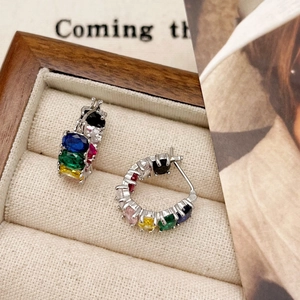 Classic silver C-shaped earrings set with multi-colored gemstones on a fabric display