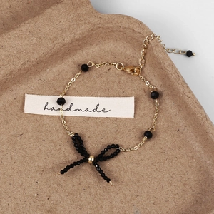 Dettaglio di un bracciale artigianale con perline nere, fiocco e catena dorata