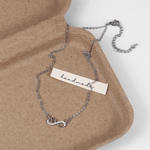Détail du collier pendentif cœur infini argenté avec strass dans un plateau en papier