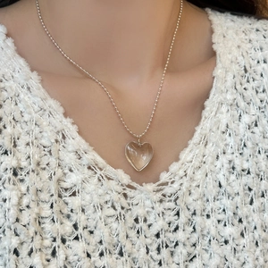 Nahaufnahme eines klaren Kristallherz-Anhängers an einer silbernen Kugelkette am Model