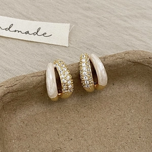 Détail de boucles d'oreilles C dorées avec émail blanc et rangées de pierres zircons