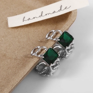 Macro detail of silver chain earrings featuring square-cut emerald green gemstones