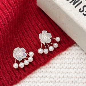 Macro detail of floral pearl earrings on red and white knit fabric backdrop