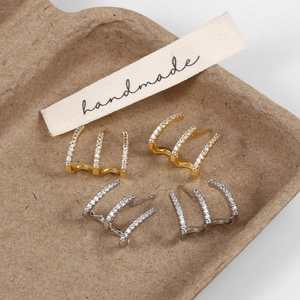 Detail showing gold and silver three-claw stud earrings with shimmering micro zircons