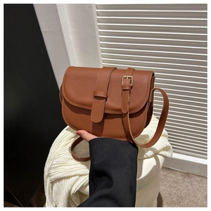 Detail of a brown caramel faux leather saddle bag with adjustable strap and metal buckle