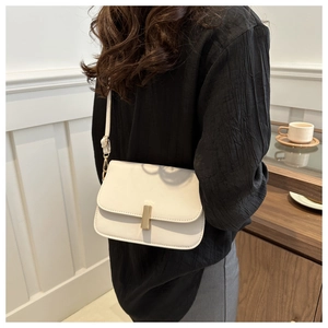 Petit sac à bandoulière blanc avec boucle dorée présenté dans un café cosy