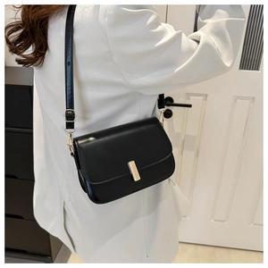 Détail d'un sac bandoulière en similicuir noir avec boucle dorée sur un blazer blanc