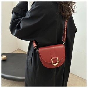 Detail of red saddle bag with gold U-buckle and textured wide shoulder strap