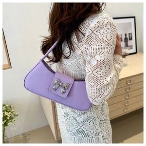 Detail of a purple baguette bag with a silver metal bow accent worn on shoulder