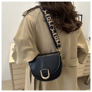 Detail of black saddle bag with golden horseshoe buckle and patterned wide strap