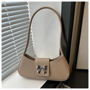 Detailed shot of beige baguette bag featuring a silver metal bow accent and smooth PU leather