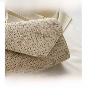 Close-up of woven straw bag with delicate pink floral embroidery and gold metal buckle