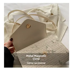 Detail of floral embroidery and magnetic snap closure on a woven straw crossbody bag