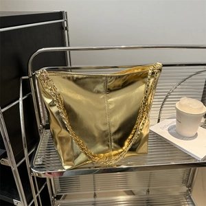 Metallic gold tote bag with chain strap displayed on shelf with coffee and books