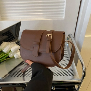 Classic brown saddle bag with golden hardware and adjustable strap in a workspace setting
