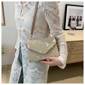 Gros plan du sac enveloppe tressé beige avec broderie florale blanche et verte