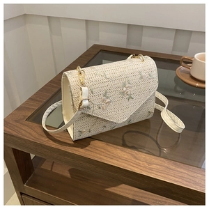 Detailed embroidery of light green and pink flowers on cream woven crossbody bag