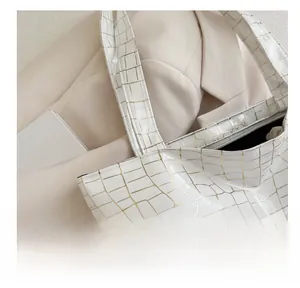 Macro detail of white glossy tote bag with golden crocodile texture and premium stitching