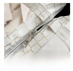 Close-up of smooth silver metal zipper and crocodile pattern on white leather bag