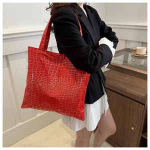 Side view of large red patent leather tote with gold crocodile texture on model