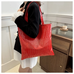 Macro detail of red tote bag with glossy crocodile texture and gold embossed finish