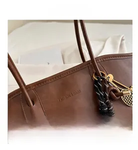 Close-up of brown pebbled leather tote with tennis racket charm and rope detail