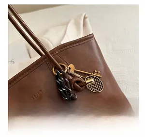 Close-up of brown leather tote with retro key and tennis racket bag charm details