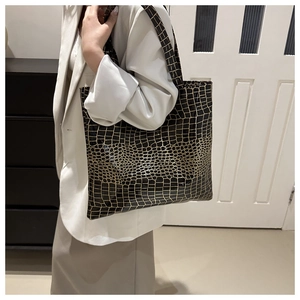 Detail shot of a large tote bag featuring gold crocodile texture worn by a model