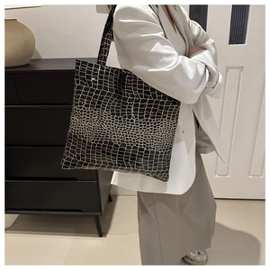 Close-up of a large black tote bag with gold texture and shiny crocodile leather pattern