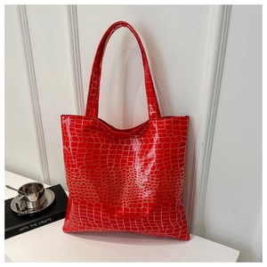 Detail of red tote bag with crocodile texture and glossy finish on a white surface