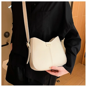 Detail of cream crossbody bag with wavy opening and fashion metal plate on dark outfit